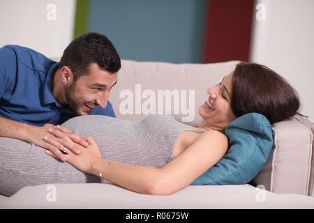 Avenir heureux papa écoute le ventre de sa femme enceinte tout en vous relaxant sur le canapé à la maison Banque D'Images