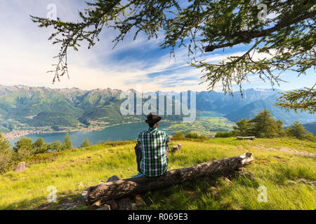 Man sitting on tree trunk regarde vers le lac de Côme et Alto Lario, Monte Legnoncino, province de Lecco, Lombardie, Italie, Europe Banque D'Images