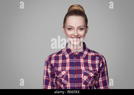 Portrait de satisfait belle fille blonde en chemise à carreaux roses recueillies bun hairstyle et un miroir et permanent à la recherche à l'appareil photo avec smil dentelée Banque D'Images