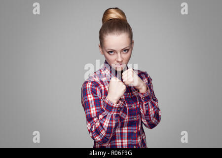 Une belle fille blonde en rouge, rose chemise à carreaux, recueillis, maquillage coiffure chignon et permanent à la caméra au poing avec attac et boxe Banque D'Images