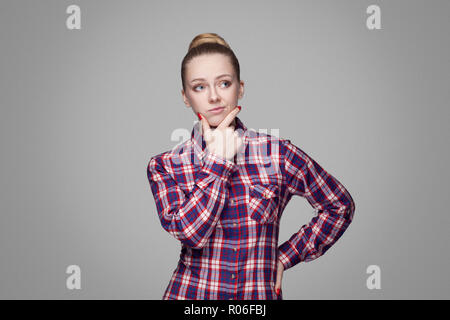 Confondre belle fille blonde en rouge, rose chemise à carreaux, recueillis, maquillage coiffure chignon et permanent à l'écart, de toucher son visage et de la pensée Banque D'Images