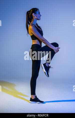 Portrait de profil de caucasian woman with slim corps solide faisant d'entraînement et s'étend ses jambes sur fond coloré isolé Banque D'Images