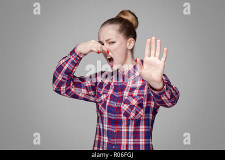 Angry blonde en rouge, rose chemise à carreaux, recueillis, maquillage coiffure chignon et permanent à la caméra à l'arrêt avec le geste et de pincer son nez Banque D'Images