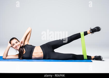 Femme l'exercice de faire d'entraînement pour les jambes avec des bandes élastiques situées sur le plancher sur fond blanc Banque D'Images