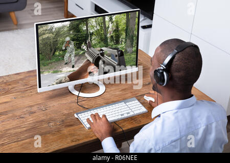 Jeune homme africain jouer l'action jeu sur ordinateur bureau en bois Banque D'Images