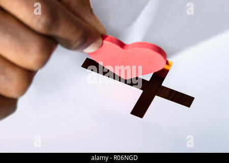 Close-up de la main d'un homme de l'insertion en forme de coeur rouge fente Crucifix Banque D'Images