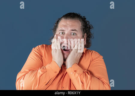 Gros homme en chemise orange détient ses mains sur son visage Banque D'Images