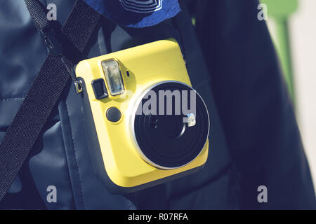 Gros plan horizontal de l'enfant avec un gilet bleu tenant un appareil photo instantané jaune autour du cou Banque D'Images