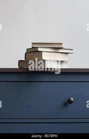 Voir le détail avant verticale de la pile livres fermés sur bleu vintage commode en bois avec poignées noires contre le mur dans la lumière naturelle copyspace Banque D'Images