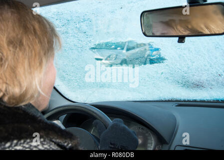 La femme est à la recherche d'une voiture par un petit écart rayé dans un pare-brise glace Banque D'Images