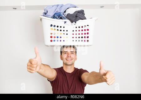 Jeune homme au sourire holding panier plein de vêtements sur la tête. Travaux domestiques après le travail, ok sign Banque D'Images
