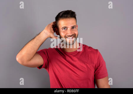 Un beau jeune homme dans un tee-shirt rouge, debout devant un fond gris dans le studio. Banque D'Images