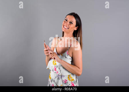 Une belle jeune femme en utilisant son smartphone devant un fond gris dans un studio. Banque D'Images