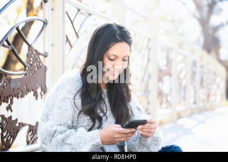 Belle jeune hispanique, American Indian, multi-raciale Femme Consultation des messages et prendre des autoportraits avec téléphone cellulaire à l'extérieur sur un jour d'automne Banque D'Images
