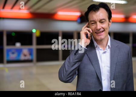 Portrait of mature handsome businessman talking on phone en gare Banque D'Images