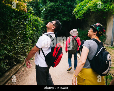 Les touristes chinois avec des sacs jusqu'à Oxford dans un jardin. Une vieille dame porte un chapeau de la marijuana Banque D'Images