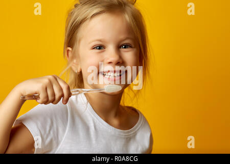 La charmante petite fille en t-shirt blanc nettoyer les dents avec des brosses à dents pour enfants regardant la caméra Banque D'Images