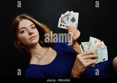 Young woman portrait sur fond noir. Modèle féminin tenu cinq cartes de poker et de l'argent, les dollars et les billets en euros. Banque D'Images