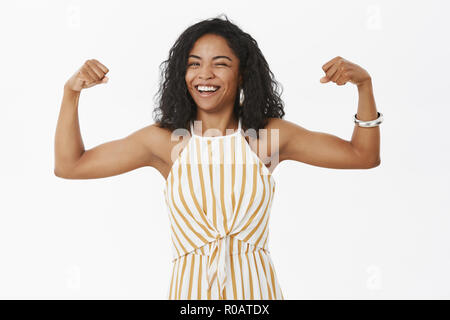 Elle peut traiter les problèmes. Portrait d'une forte et joyeuse independet african american élégant de la sportive working out in gym debout dans des combinaisons et montrant les muscles et clignant smiling Banque D'Images