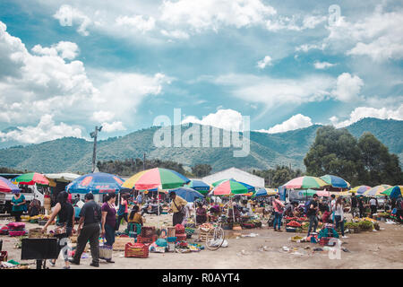 Les étals de marché alimentaire dynamique disposés sur le sol par des femmes en tenue traditionnelles mayas sous un parasol parasols colorés à Antigua, Guatemala Banque D'Images