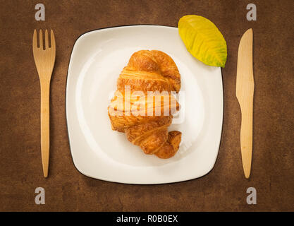 Croissant sur une assiette décorée avec des feuilles d'automne, sur fond de cuir brun. Banque D'Images