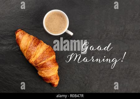 Bon matin bannière. Une photo d'un croissant et une tasse de café, tourné à partir de ci-dessus, sur un fond noir avec copie espace Banque D'Images