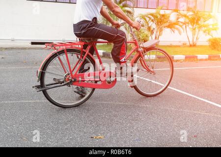 Close up homme monter une bicyclette classique rouge vintage dans ancien beau coucher de soleil avec ton léger Banque D'Images