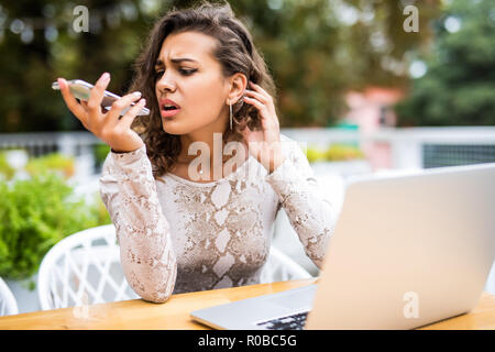 Belle femme parle sur un téléphone mobile tout en restant assis dans le bureau avec un ordinateur portable. Jeune fille est indépendant à l'appelant les clients et lecture em Banque D'Images