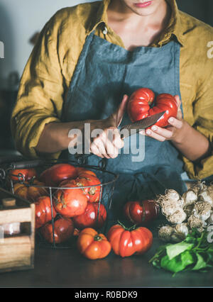 Tablier en lin femme mûre heirloom tomato coupe et la cuisson de la sauce tomate, tomates en conserve ou de pâtes au basilic et l'ail au comptoir de la cuisine. En bonne santé Banque D'Images