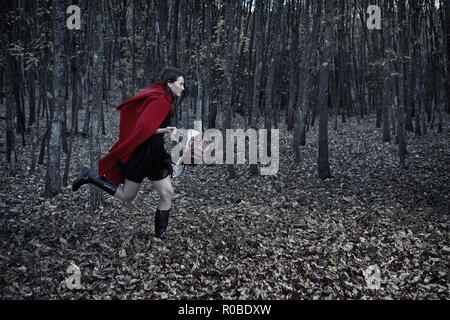 Femme habillée en Chaperon Rouge courir de nuit à travers la forêt Banque D'Images