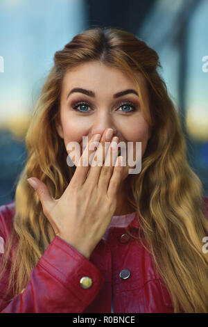 Closeup portrait of belle blonde pensive white Caucasian girl femme, portée à l'extérieur de red jacket in city street, style portrait concept Banque D'Images