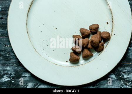 Doux, truffes au chocolat et cacao amer sur une assiette blanche et un arrière-plan sombre Banque D'Images