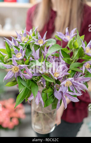 Bouquet de lilas clematis fleurs dans vase en verre. Le travail de la fleuriste à un magasin de fleur. Un vase en verre avec des fleurs placées sur le tableau gris en bois Banque D'Images