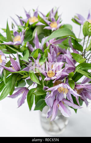 Bouquet de lilas clematis fleurs dans vase en verre. Le travail de la fleuriste à un magasin de fleur. Un vase en verre avec des fleurs placées sur le tableau gris en bois Banque D'Images