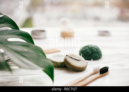 Eco friendly bambou naturel brosses à dents, dentifrice, shampoing bar en verre, brosse en bois et bois blanc sur éponge konjaku avec feuilles vert monstera. Banque D'Images