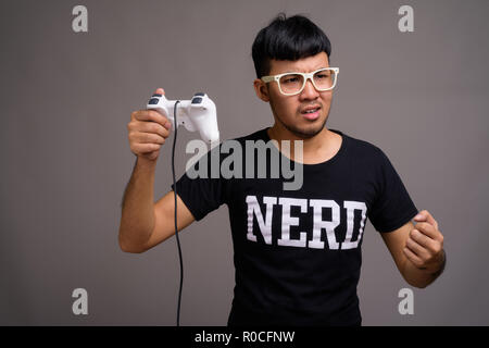 Jeune homme portant des lunettes nerd asiatique contre l'arrière-plan gris Banque D'Images