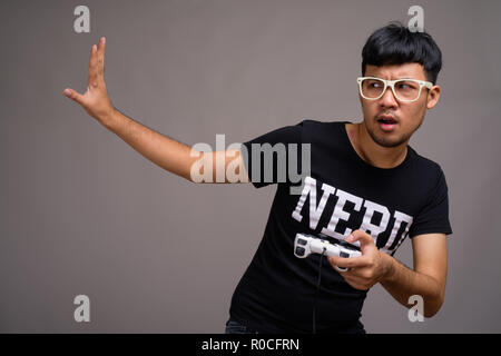 Jeune homme portant des lunettes nerd asiatique contre l'arrière-plan gris Banque D'Images