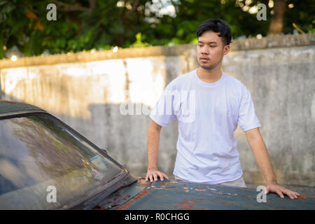 Young Asian man avec vieille voiture rouillée dans les rues à l'extérieur