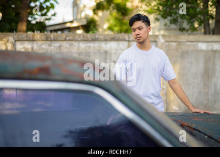 Young Asian man avec vieille voiture rouillée dans les rues à l'extérieur