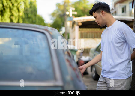 Young Asian man avec vieille voiture rouillée dans les rues à l'extérieur Banque D'Images