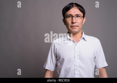 Jeune homme portant des lunettes nerd asiatique contre l'arrière-plan gris Banque D'Images