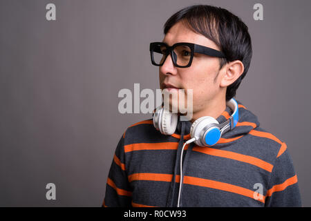 Young Asian nerd man wearing hoodie et écouteurs contre gray Banque D'Images