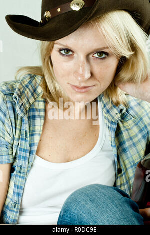 Jolie femme occidentale en chemise de cow-boy et un chapeau avec une bouteille de whisky Banque D'Images