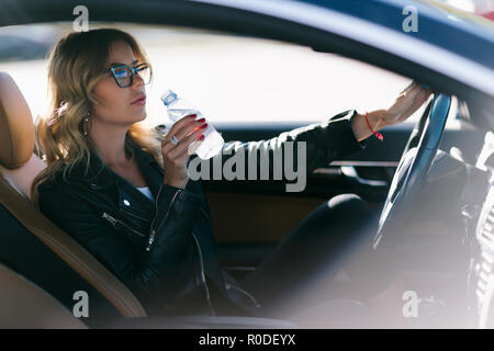 Photo de jeune femme avec bouteille d'eau dans sa main sitting in car Banque D'Images