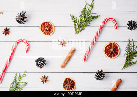 Schéma des bonbons de Noël, des pommes de pin et des oranges séchées sur fond de bois blanc. Décorations de Noël Banque D'Images