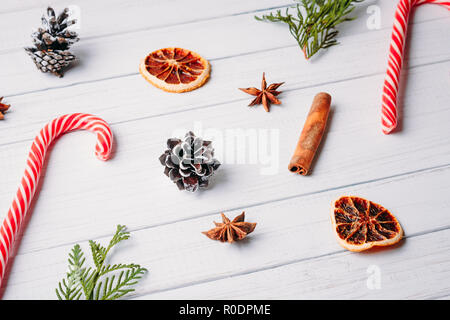 Schéma des bonbons de Noël, des pommes de pin et des oranges séchées sur fond de bois blanc. Décorations de Noël Banque D'Images