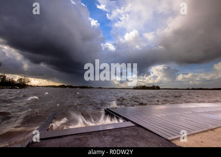 Des nuages sombres et vent modéré élevé vagues se brisant sur un débarcadère quand une tempête s'en vient en plus d'un Dutch lake Banque D'Images