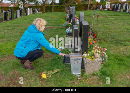 Blonde mature dame supprime les fleurs mortes provenant d'une tombe et dit une prière pour son père Banque D'Images