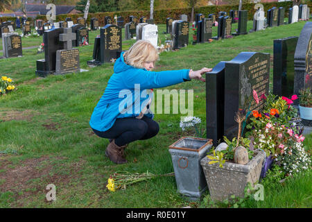 Blonde mature dame supprime les fleurs mortes provenant d'une tombe et dit une prière pour son père Banque D'Images