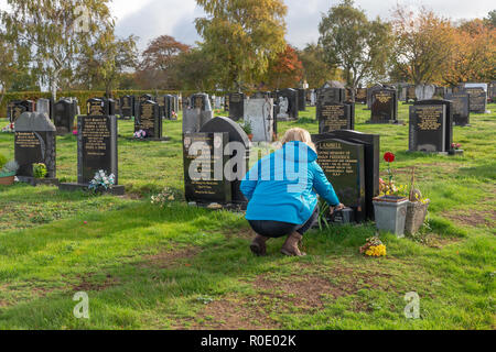 Blonde mature dame supprime les fleurs mortes provenant d'une tombe et dit une prière pour son père Banque D'Images